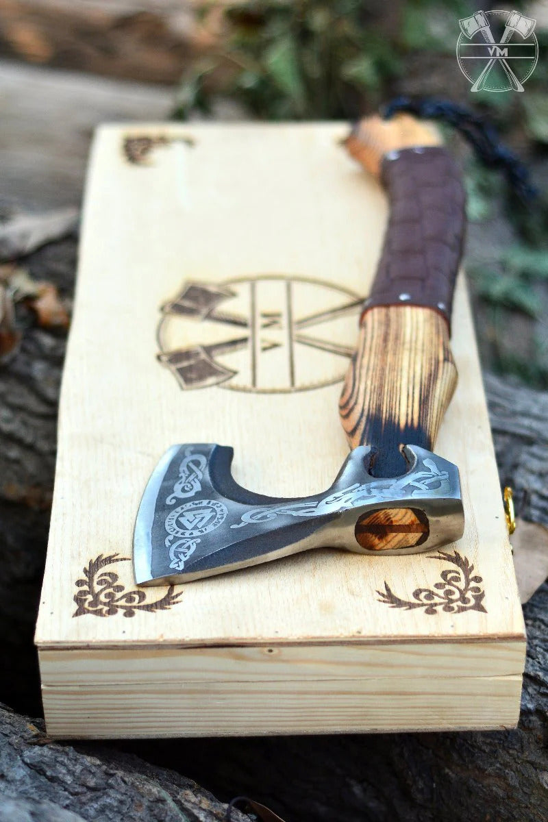 Valknut Viking Axe with blade and wooden handle on a wooden box with laser cut design, outdoors.