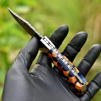Hand holding a folding knife with a wooden handle against a blurred green background