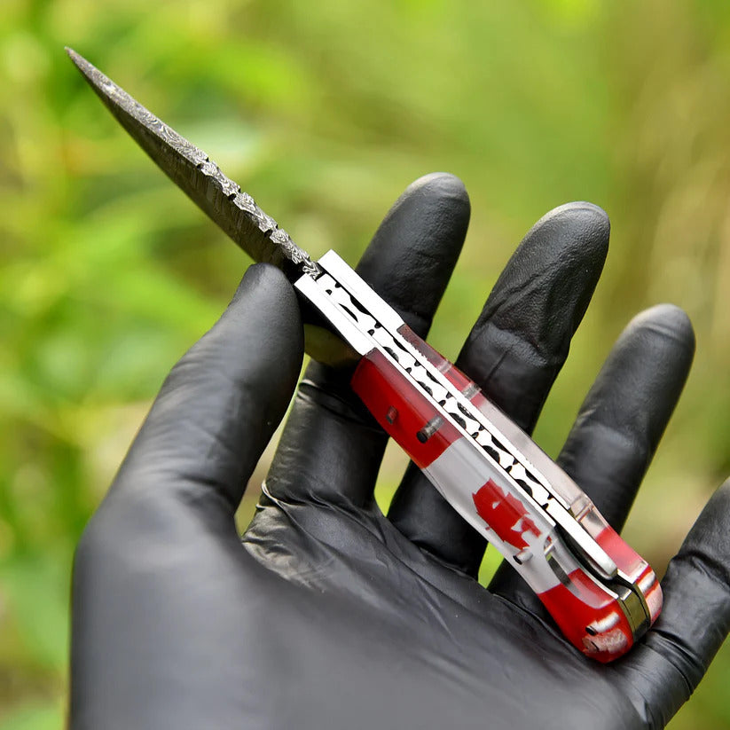 Red and silver pocket knife held by a hand in a black glove with a blurred green background