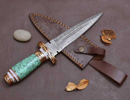 Decorative knife with a blue resin handle and gold accents on a brown surface with leaves and a stone.