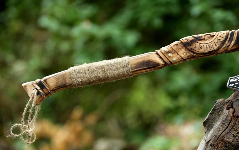Wooden staff with carved details and twine wrapping, against a blurred natural background