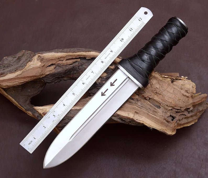Long horfinn dagger Knife with a black handle on a wooden block next to a ruler for scale.