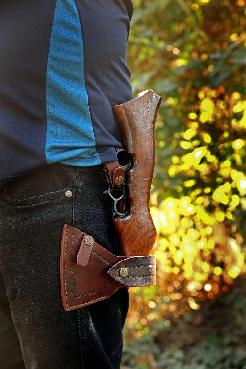 Person wearing a Knuckle Viking Axe with a rifle against a blurred natural background