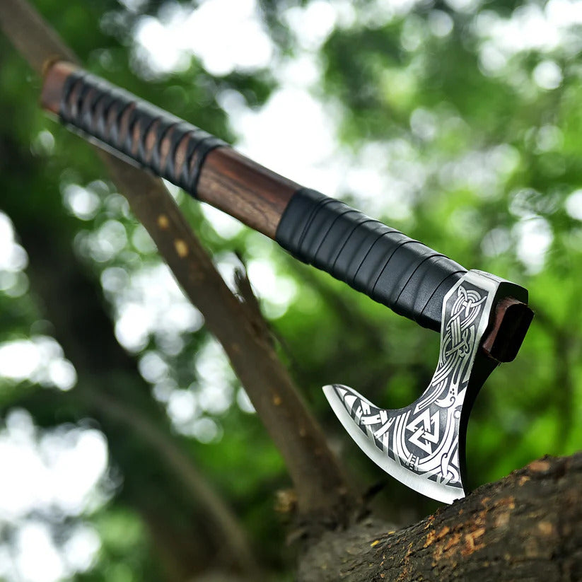Decorative axe with a black handle and silver blade on a wooden surface with a blurred green background