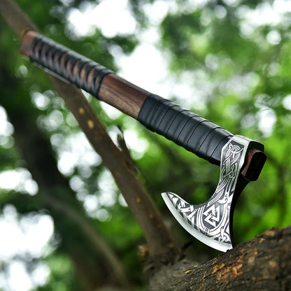 Decorative axe with a black handle and silver blade on a wooden surface with a blurred green background
