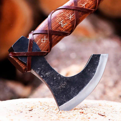Wooden-handled of  Authentic Handmade Viking Axe with decorative carvings on a blurred natural background