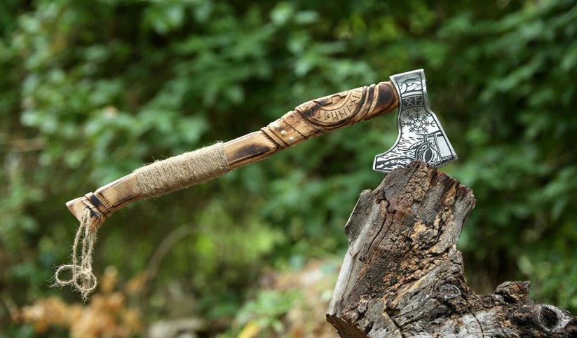 Wooden-handled axe with a metal head on a wooden stump against a blurred green forest background