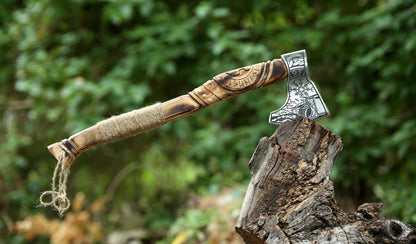 Wooden-handled axe with a metal head on a wooden stump against a blurred green forest background